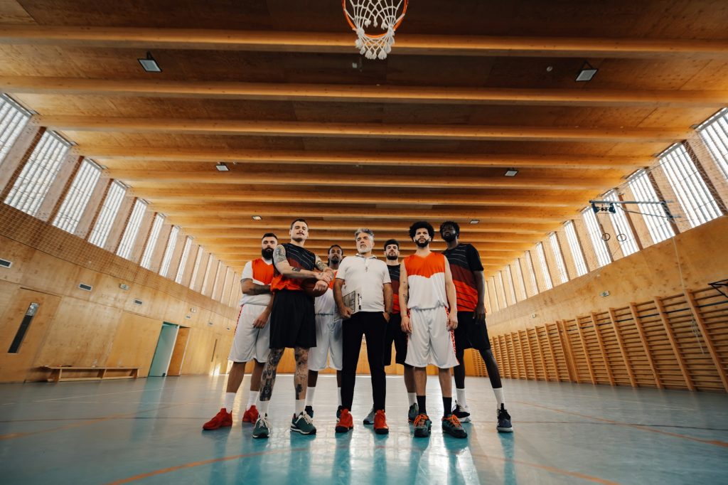 Low angle view of interracial basketball team with senior coach at court.